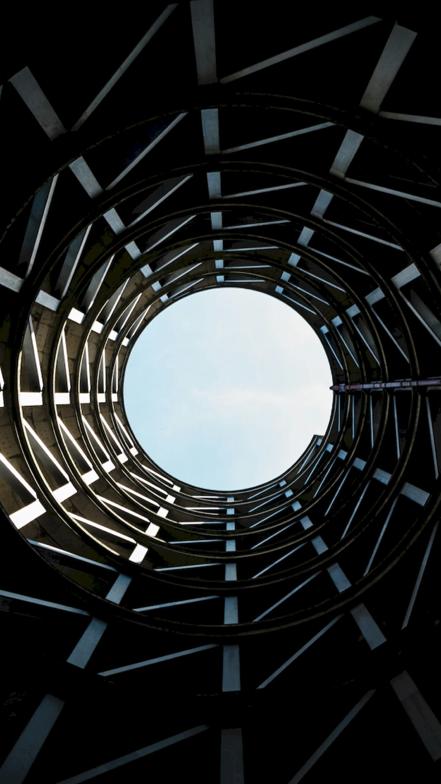 Low angle view looking up at a spiral concrete parking ramp structure with a circle of blue sky in the center.