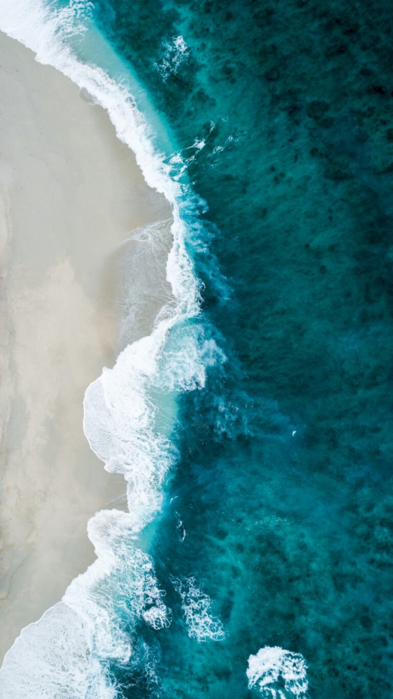 Top-down aerial view of turquoise blue ocean waves crashing on a clean white sandy beach.