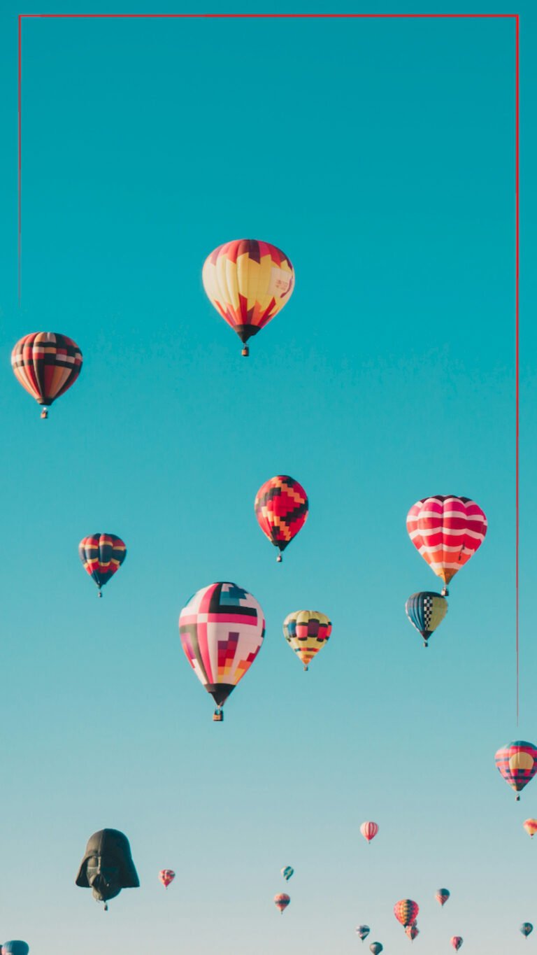 Low angle view of many colorful hot air balloons flying in a clear teal blue sky, vertical 4K phone wallpaper