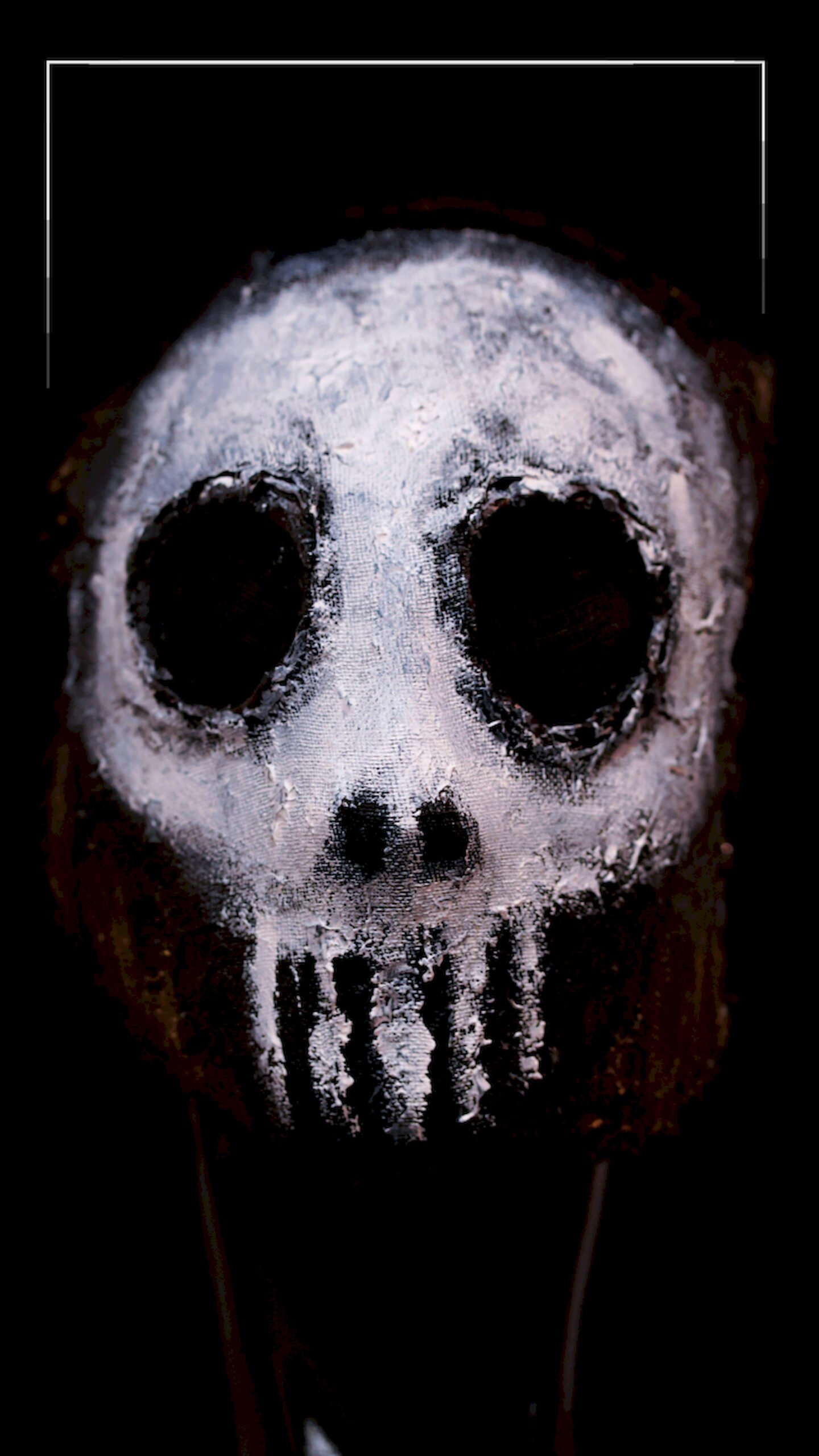 Close-up art of a white painted skull mask with rough texture and hollow black eyes against a black background.