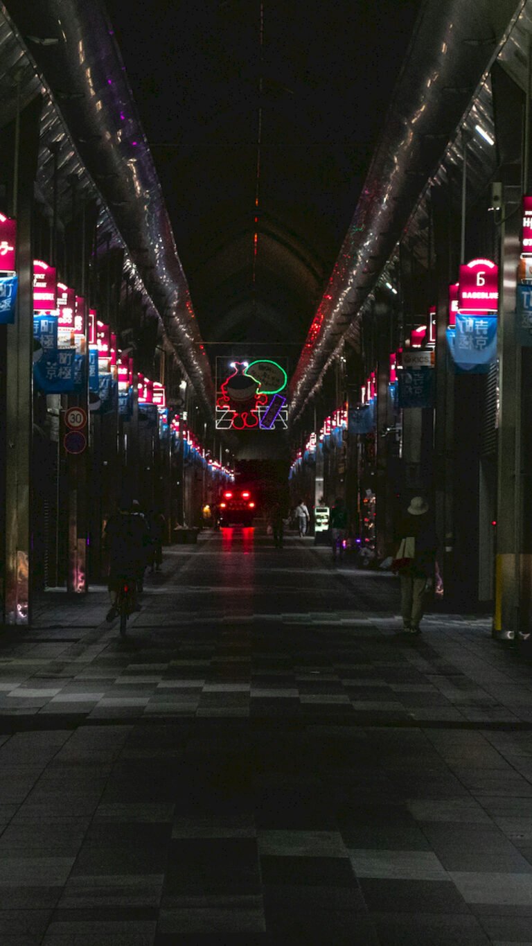 Dark vertical view of a Japanese covered shopping street at night with neon signs and people walking, 4K phone wallpaper.