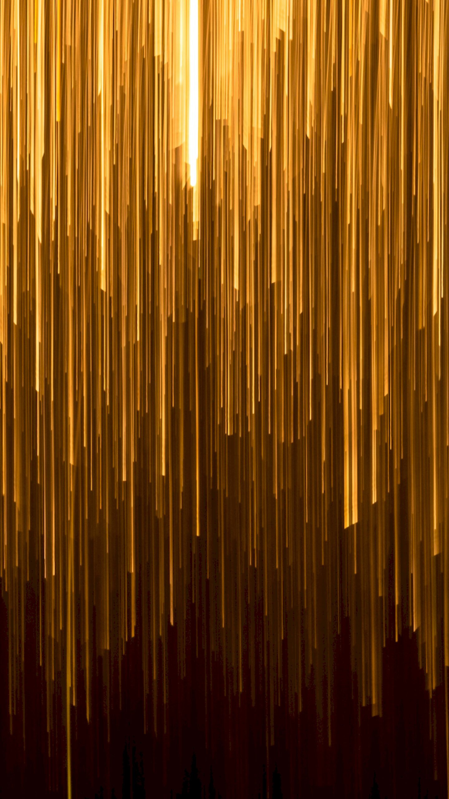 Abstract wallpaper featuring vertical streaks of bright golden light falling like rain against a dark brown and black background.