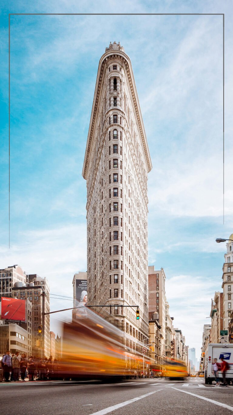 "Vertical low-angle view of a dark grey brick apartment building with balconies standing next to a modern white high-rise facade with tall narrow windows."