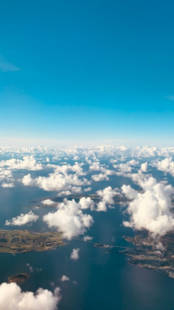 "Vertical aerial view of white clouds scattered over a blue ocean and coastline with islands and bridges, high-resolution mobile wallpaper."