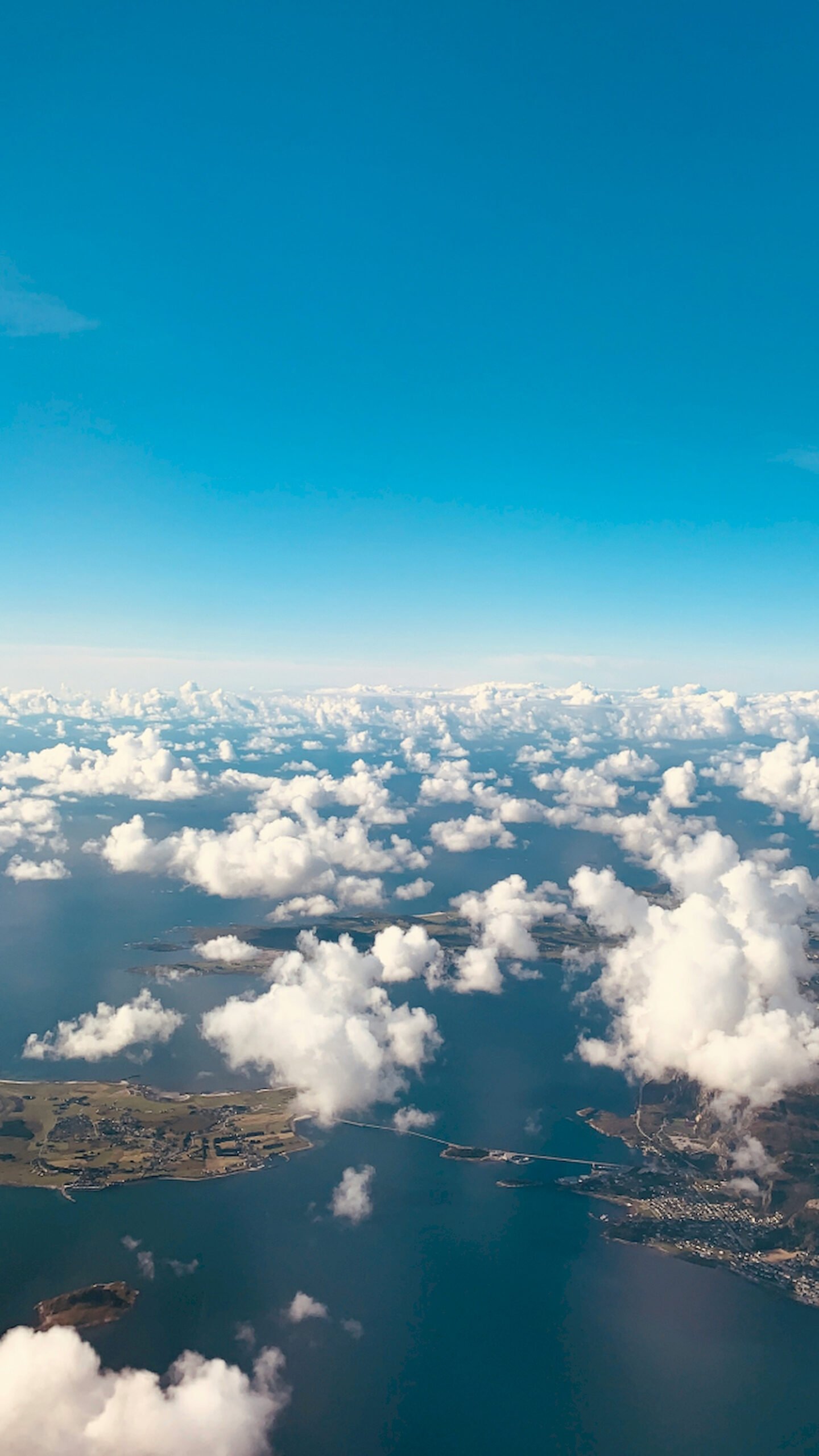"Vertical aerial view of white clouds scattered over a blue ocean and coastline with islands and bridges, high-resolution mobile wallpaper."