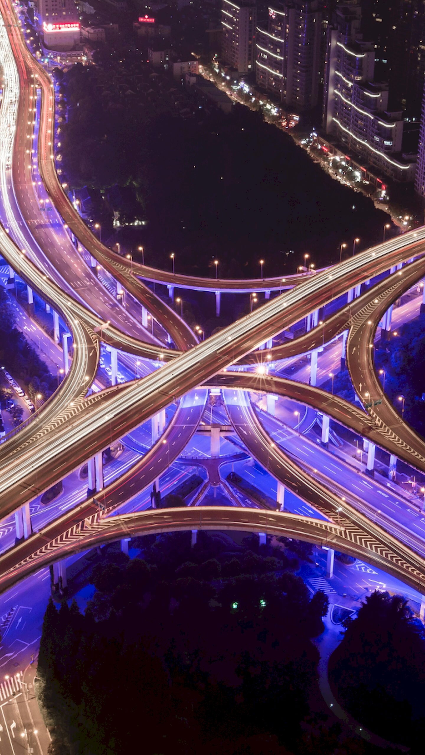 Aerial vertical view of a massive highway interchange in Shanghai at night with blue neon lights and traffic trails, 4K phone wallpaper.