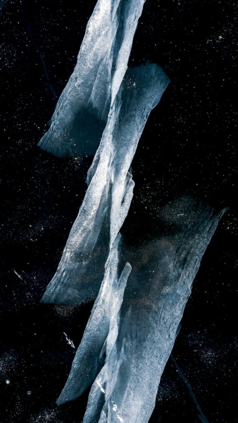 Vertical abstract wallpaper featuring sharp, jagged ice crystals or shards floating against a solid black background with scattered white specks.