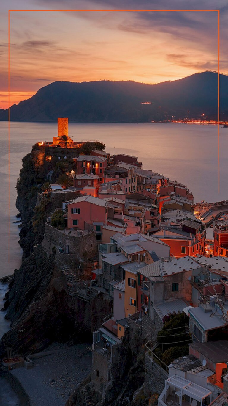 English: Aerial vertical view of Vernazza village in Cinque Terre, Italy at sunset with illuminated buildings and a tower on the cliff, 4K phone wallpaper.