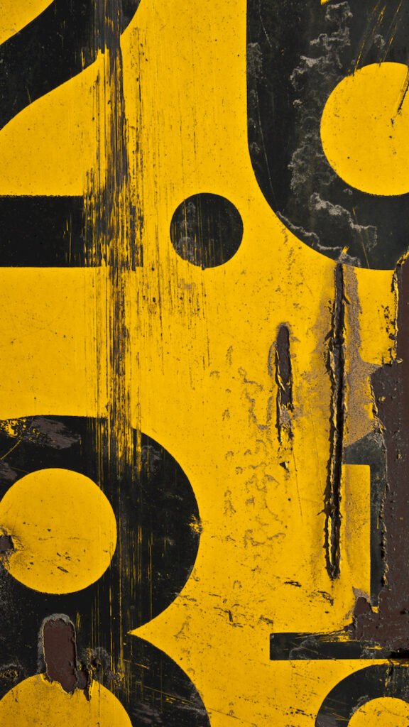 Close-up vertical texture of a yellow industrial surface featuring large, partially visible black numbers, heavy scratches, and peeling paint revealing rust underneath.