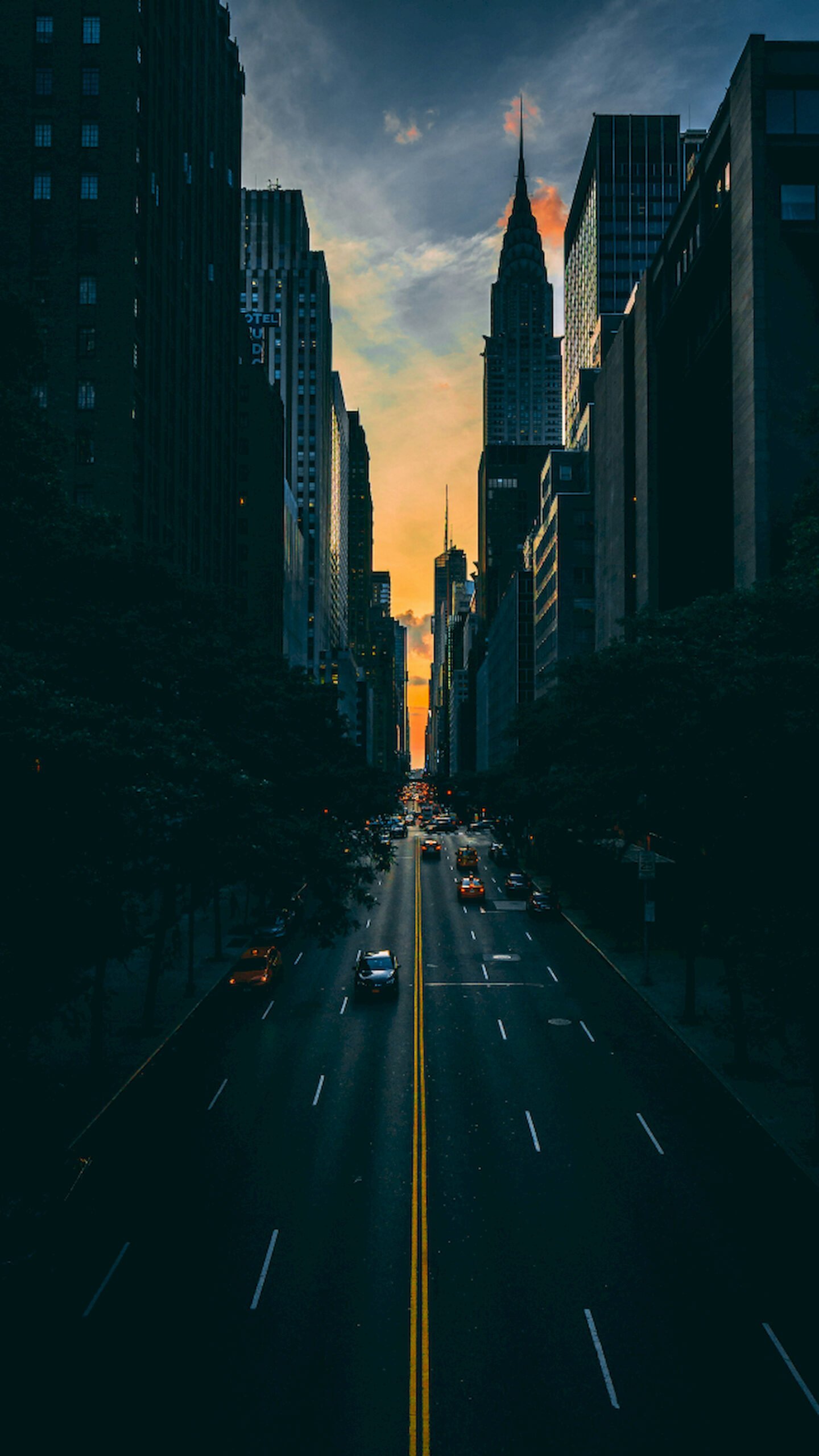 "Dark street view in New York City looking towards the illuminated Chrysler Building at sunset, vertical 4K phone wallpaper."